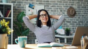Femme souriante et détendue au bureau, symbole de sérénité retrouvée grâce à l’externalisation des tâches